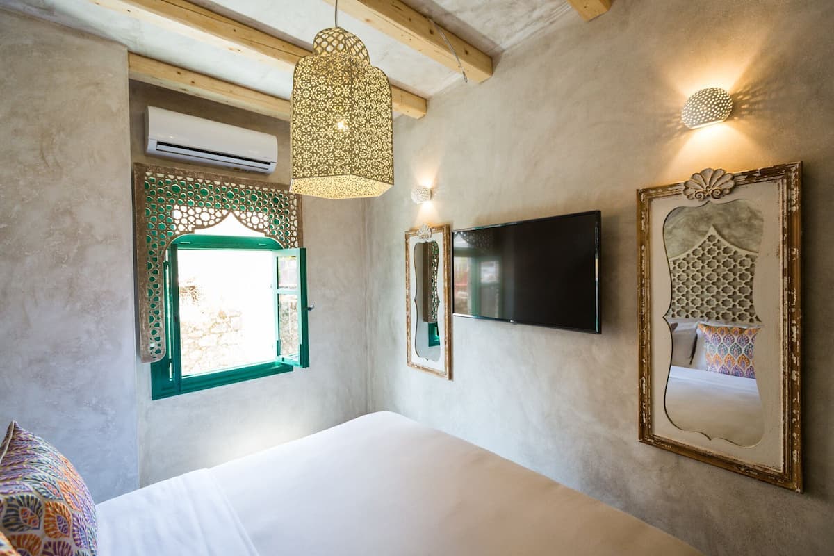 Een slaapkamer met een bed, een televisie, een spiegel aan de muur en een hanglamp.