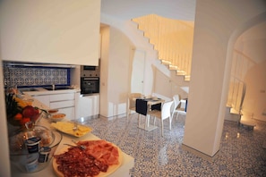 Una cocina moderna con comedor, armarios blancos, salpicadero de azulejos y una escalera que sube a un nivel superior.