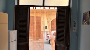 Una habitación con cocina, una mesa de comedor con mantel estampado y vista a la calle por una puerta abierta.