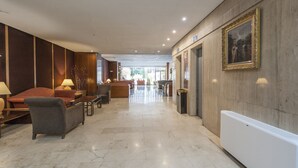 Een ruime lobby met een marmeren vloer, een receptiebalie en een zithoek met banken en stoelen.