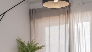 Een moderne woonkamer met een beige fauteuil, een witte vaas met een plant, een zwarte vloerlamp en dunne gordijnen.