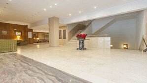Een ruime lobby met een marmeren vloer, een trap en een receptiehoek met een bank en lampen.