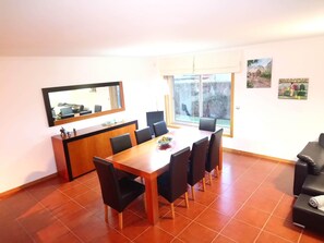 A dining area with a wooden table and black chairs, a small kitchen counter with a mirror, and a large window with a view of trees.