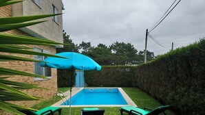 A backyard with a swimming pool, green lawn, and a blue umbrella. - Beach House - Between Porto, Braga and Viana do Castelo (Esposende)