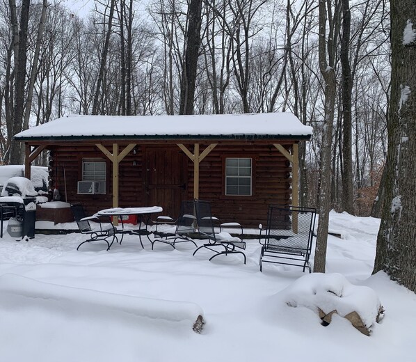 Una cabaña de madera con un porche cubierto, rodeada de árboles nevados.
