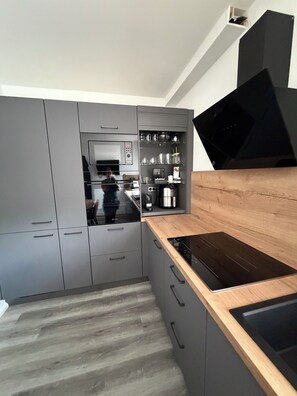 Una cocina moderna con armarios grises, encimera de madera y campana extractora negra.