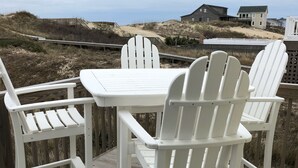Une terrasse en bois avec une table blanche et quatre chaises Adirondack blanches.