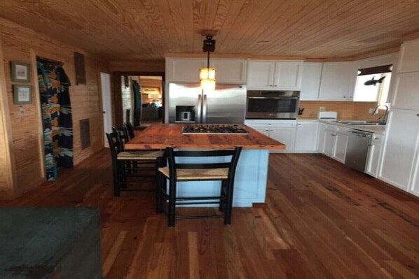 Una cocina con suelo de madera, armarios blancos, una isla central con sillas y electrodomésticos de acero inoxidable.