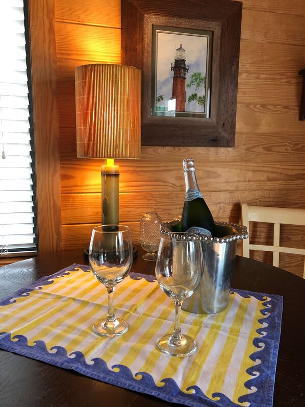 Een houten tafel met een geribbelde placemat, twee wijnglazen, een champagnefles en een kaars.