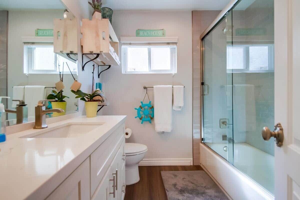 A bathroom with a large mirror, a sink, a toilet, a shower with glass doors, and a window with a sign above it.