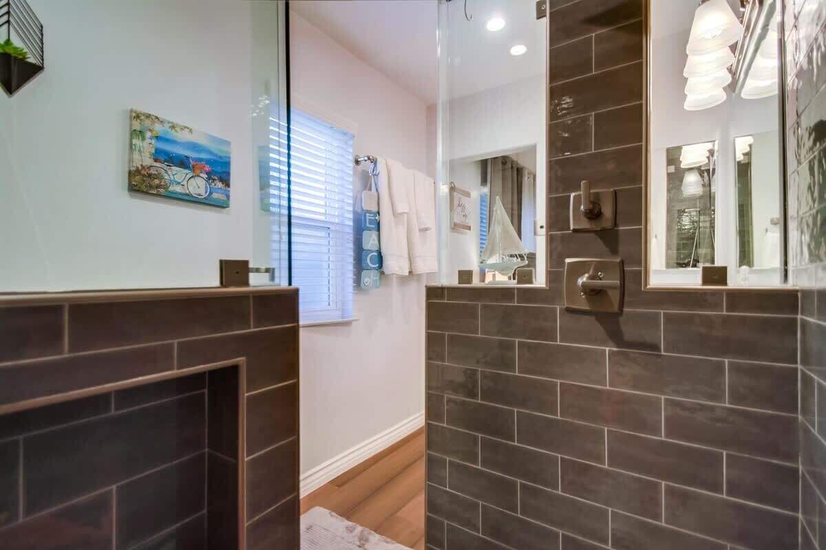 Un baño con paredes de azulejos oscuros, cabina de ducha de vidrio, un perchero y un cuadro en la pared.