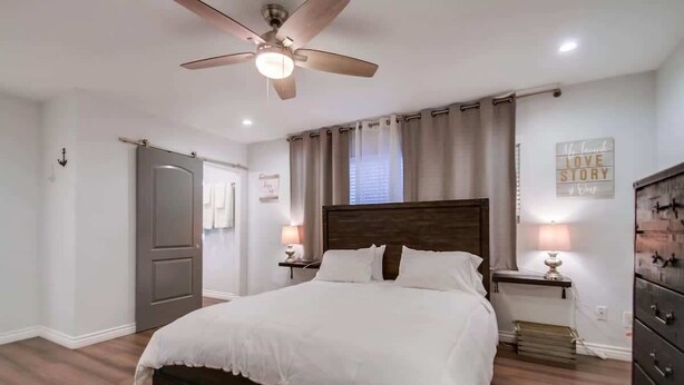 Een slaapkamer met een bed, plafondventilator, bedlampjes, een dressoir en een muur met een motiverende quote.