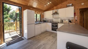 A modern kitchen with wooden ceiling and white cabinets, a built-in oven, and a large window overlooking a deck. - Lomond Lodge 20, Luxury Log cabin on the banks of Loch Lomond (Loch Lomond)