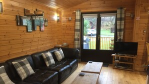 A wooden-paneled room with a black leather sofa, a wooden coffee table, and a television on a wooden stand. - Lomond Lodge 20, Luxury Log cabin on the banks of Loch Lomond (Loch Lomond)