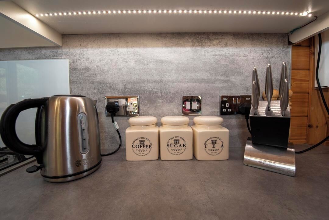 A kitchen with a kettle, coffee jars, sugar jars, and a coffee machine.