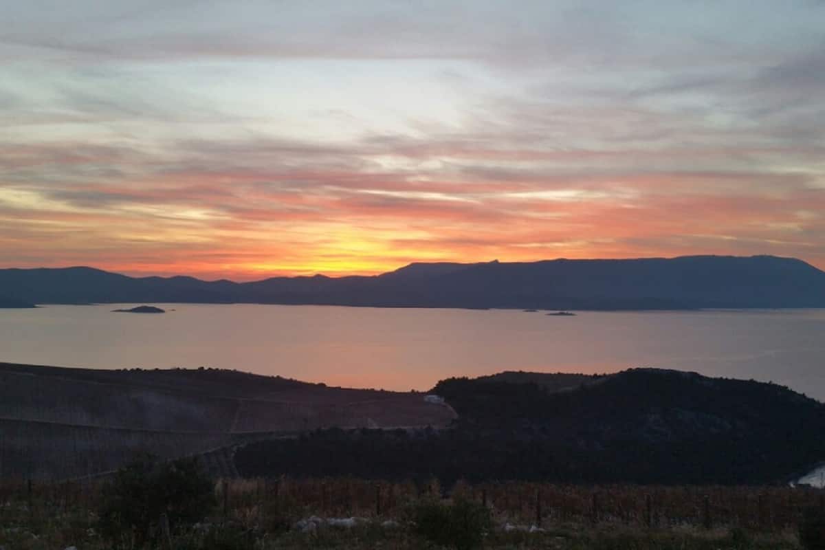 A sunset over a calm lake with distant mountains and a forested area.