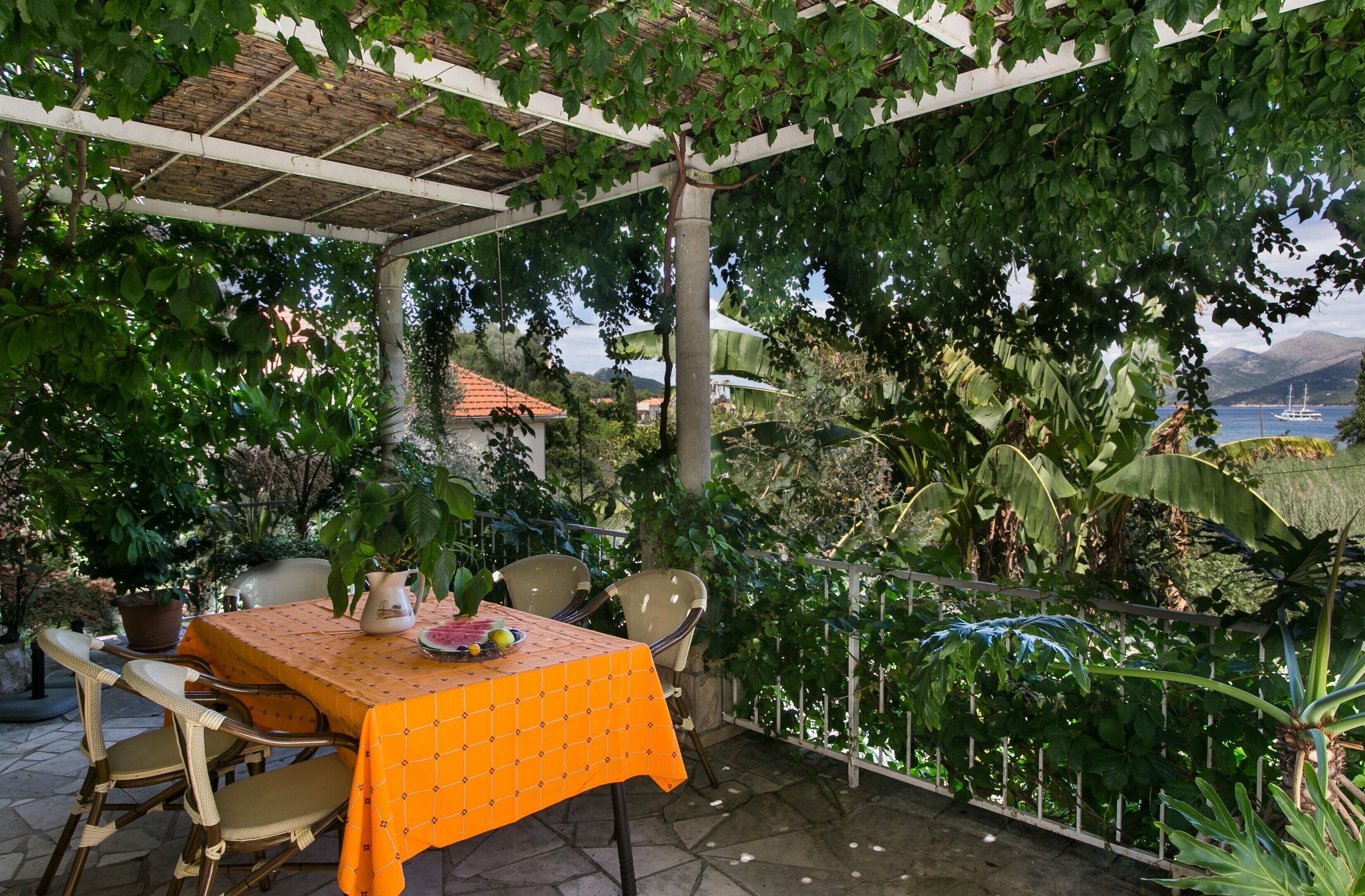 An outdoor patio with a table covered in an orange tablecloth, surrounded by wicker chairs.