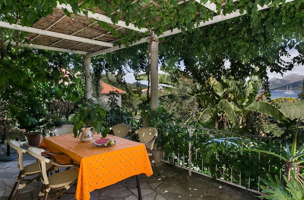 An outdoor patio with a table covered in an orange tablecloth, surrounded by wicker chairs.