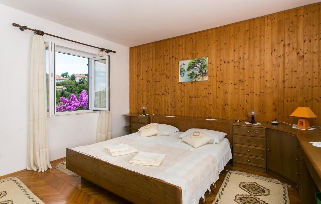 A bedroom with a wooden headboard, a bed with white linens, a nightstand, a dresser, and a window with curtains.