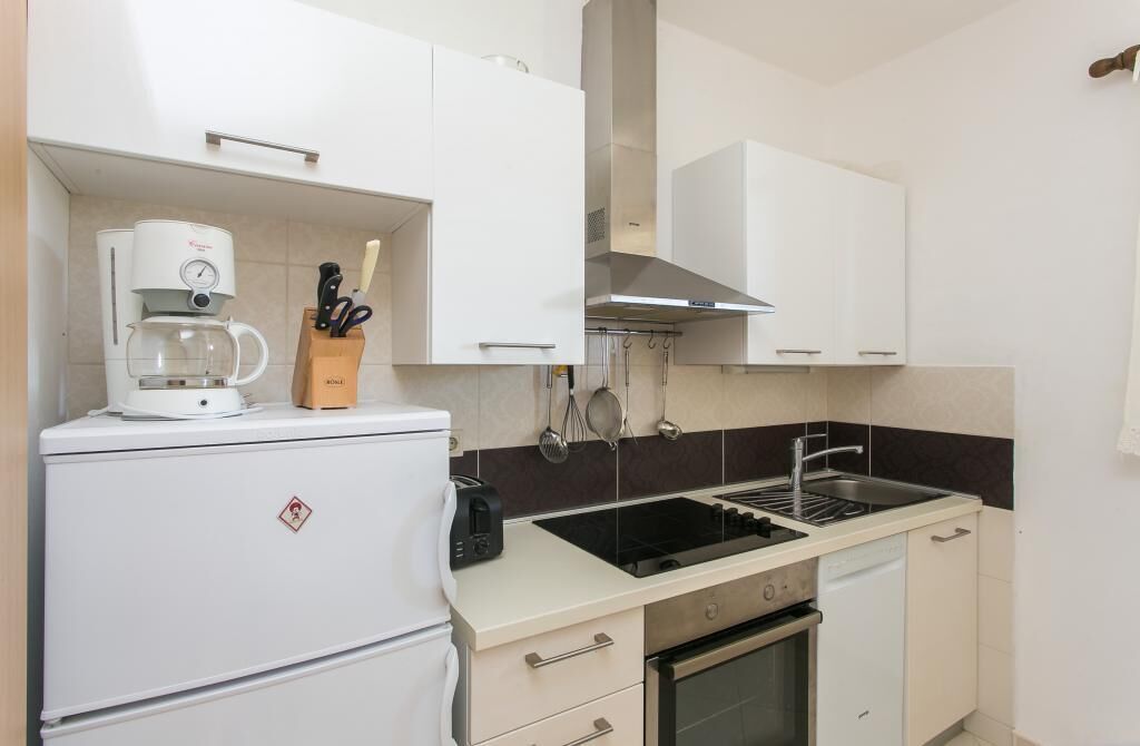 A compact kitchen with white cabinets, a coffee maker, a toaster, a sink, and a stove.
