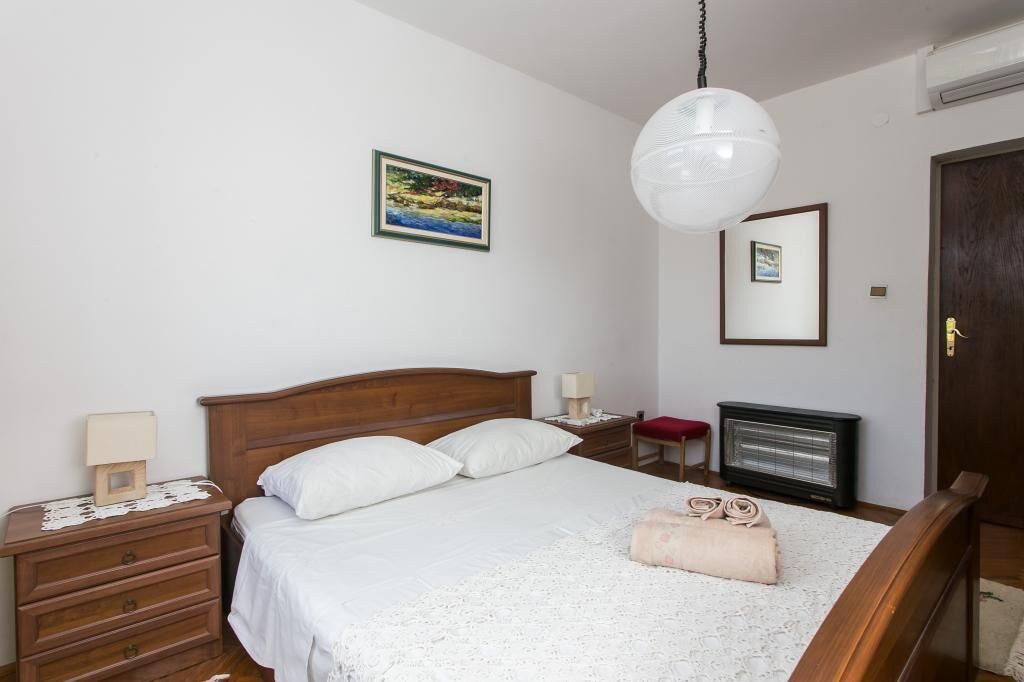 A bedroom with a wooden bed, a nightstand with a lamp, a heater, and a wall-mounted mirror.