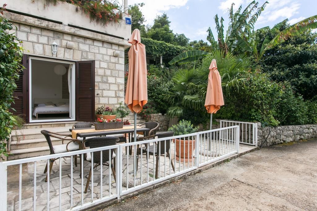 A patio with outdoor furniture and umbrellas, a stone wall, and lush greenery.