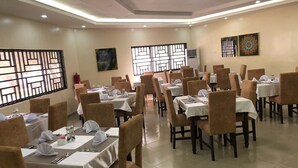 Un comedor con varias mesas dispuestas para el servicio, cada una con manteles blancos y sillas marrones.