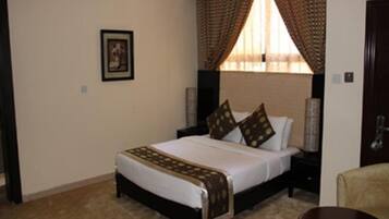 A hotel room with a large bed, a headboard with curtains, a framed picture on the wall, and a small table.