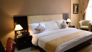 Habitación de hotel ordenada con una cama grande, dos mesitas de noche con lámparas, una silla y vistas al exterior a través de cortinas.