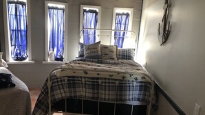 Ein Bett mit kariertem Überwurf, einem Metall-Kopfteil und einem Fenster mit blauen Vorhängen.