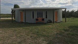 Ein kleines, eingeschossiges Haus mit einer Veranda, einer Bank und einem eingezäunten Garten.