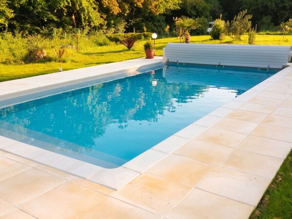 Une piscine rectangulaire à l’eau d’un bleu cristallin, entourée d’une terrasse carrelée et d’une végétation luxuriante.