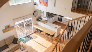 Een moderne keuken met een centraal eiland, een eethoek met een houten tafel en barstoelen, een bank en een trap.