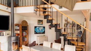 Een ruime kamer met een grote eettafel, een open haard, boekenkasten, een wereldkaart en een spiltrap.