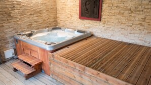 Een hottub met houten trap en houten terras, gelegen tegen een stenen muur met een Boeddhabeeld.