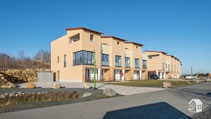 Un immeuble résidentiel moderne à plusieurs étages, doté de grandes fenêtres et de balcons, d’un mur de soutènement en pierre et d’une allée pavée.