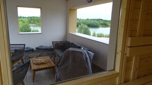 Une pièce chaleureuse avec un plafond en bois, deux fenêtres donnant sur un lac, un canapé, une table et deux chaises.