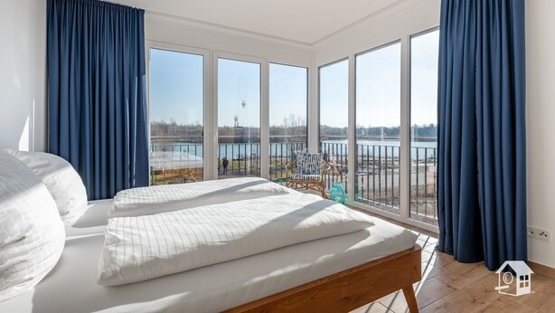 Une chambre avec une grande fenêtre, un lit et une vue sur une étendue d’eau.