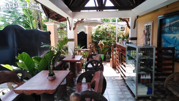 Un espace café en plein air avec des tables et des chaises en bois, entouré de plantes en pot et doté d’un sol carrelé.