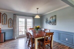 Une salle à manger avec une table et des chaises en bois, un vase rempli de fleurs et un tableau accroché au mur.