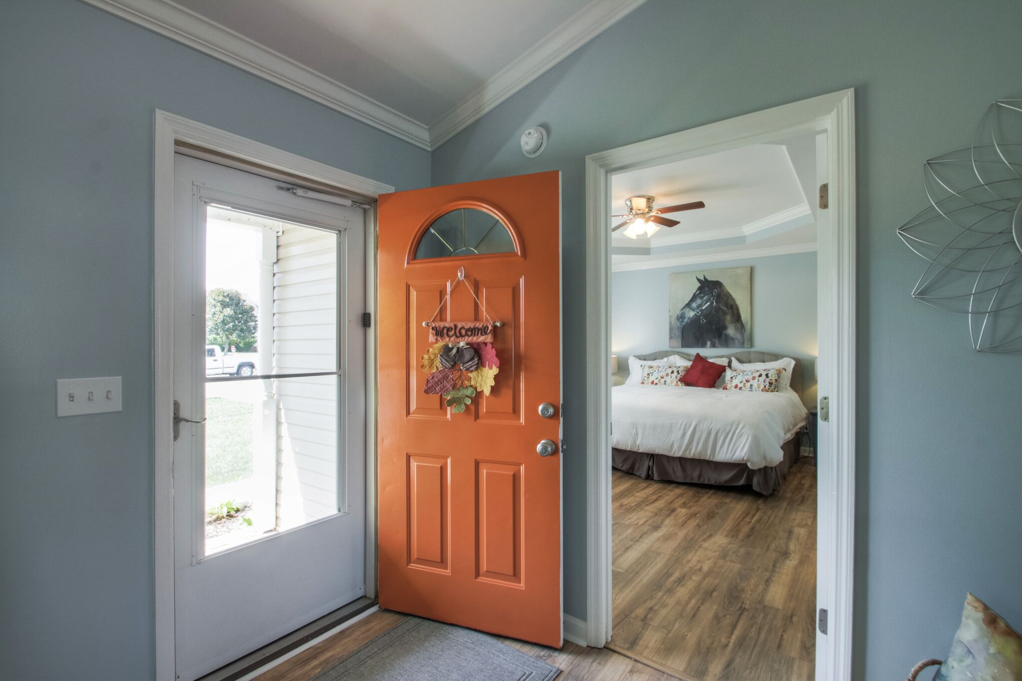 Une chambre avec un lit, un ventilateur de plafond et une pancarte de bienvenue sur la porte.