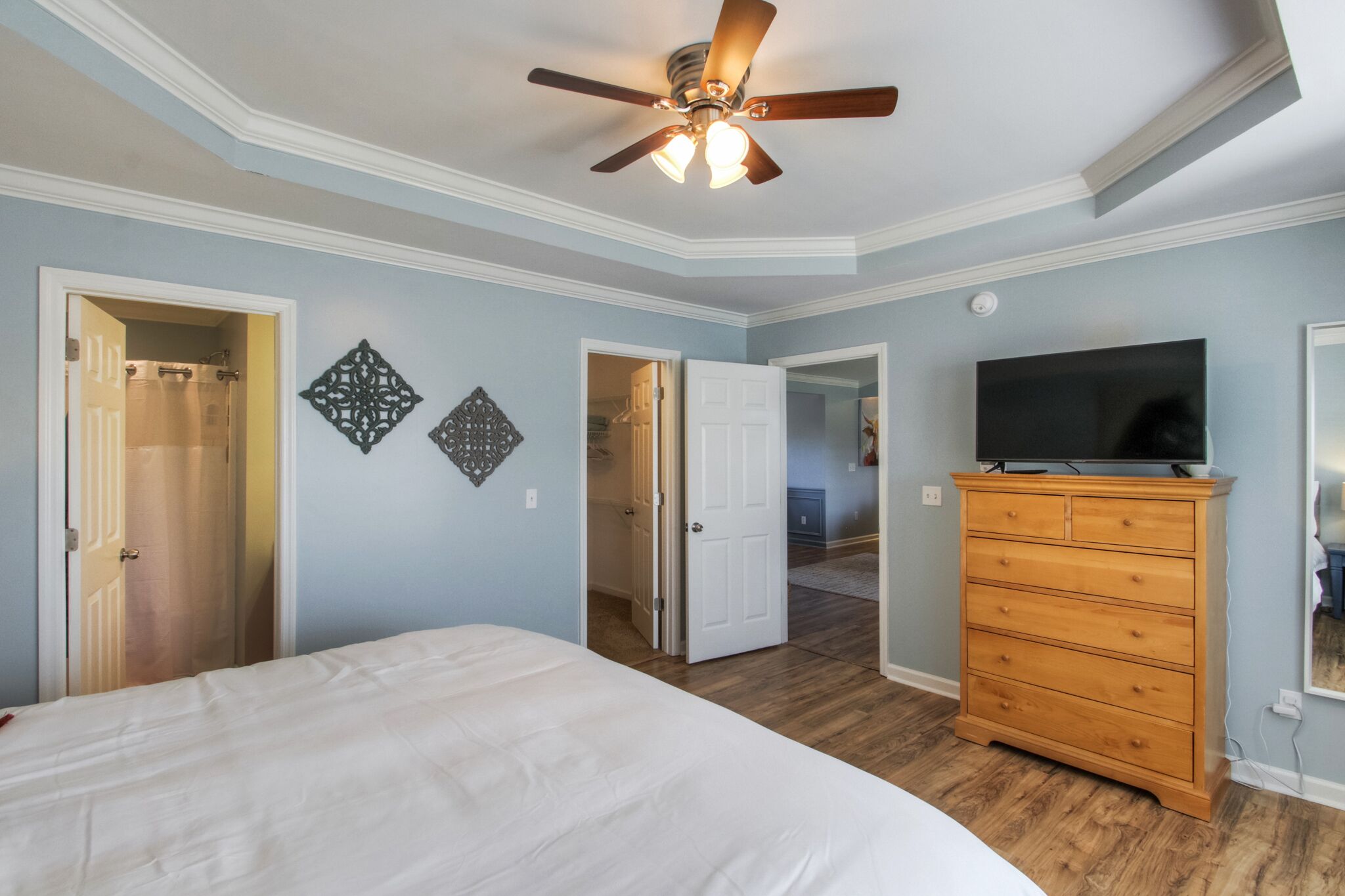 Un dormitorio con una cama, un aparador de madera, un ventilador de techo y un televisor.