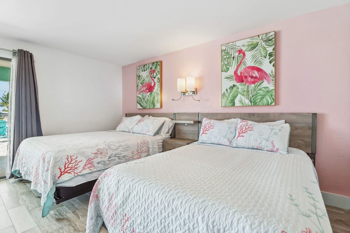 A hotel room with two beds, a wooden headboard, and two wall-mounted lamps.