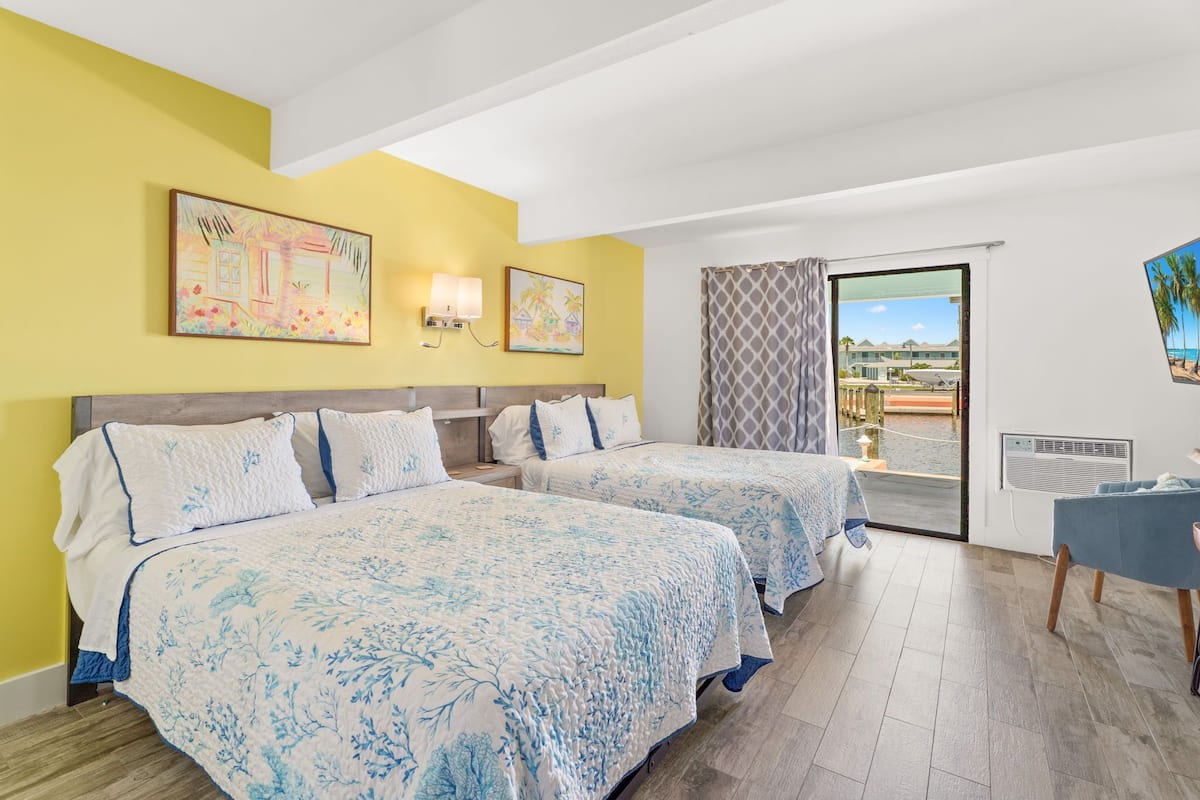 A hotel room with two beds, a balcony with a view, and artwork on the walls.