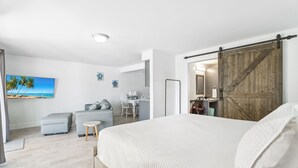 Een slaapkamer met een groot bed, een bureau en een stoel. Er is een schuifdeur en een schilderij van een strand aan de muur.