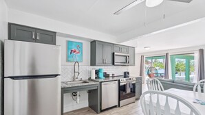 Een moderne keuken met grijze kastjes, een roestvrijstalen koelkast, een magnetron en een spoelbak. Op de muur hangt een schilderij van een flamingo.