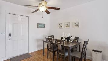 A dining area with a ceiling fan, a white door, and a small trash bin.