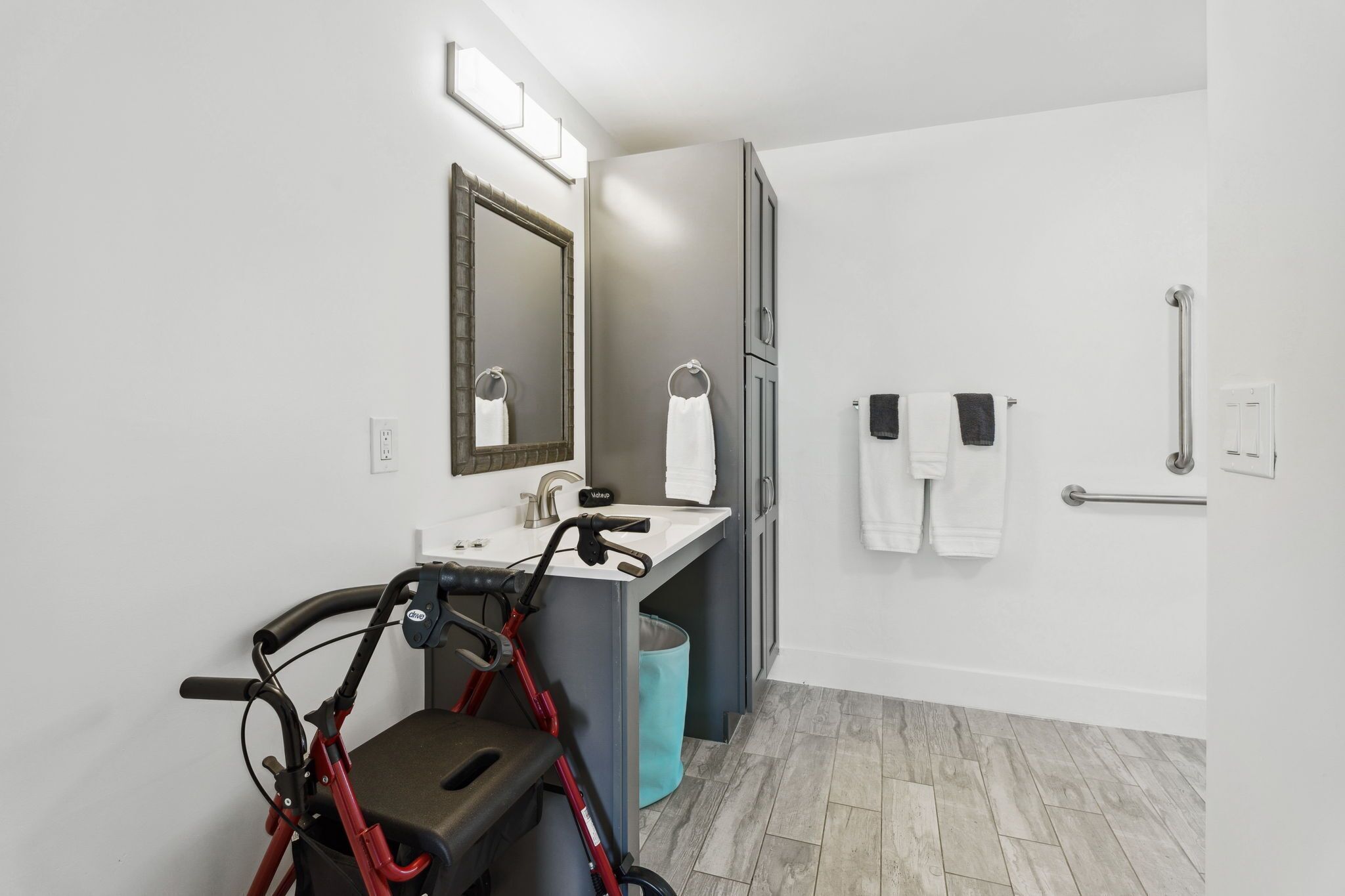 A modern bathroom with a wheelchair, a sink, a mirror, and a shower area.