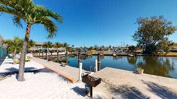 A marina with docked boats, a barbecue grill, and a sandy beach area with palm trees.