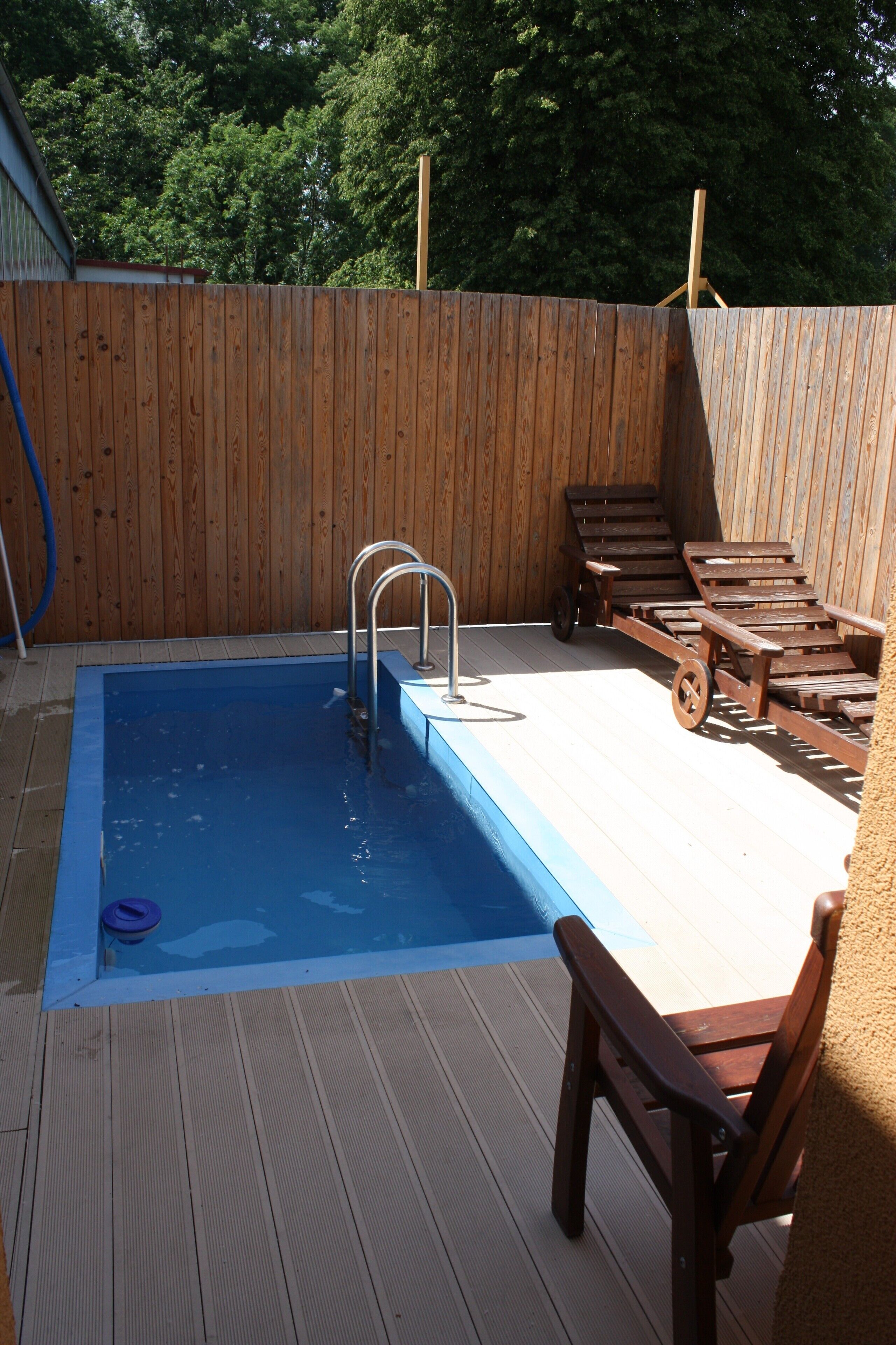 A rectangular pool with a metal ladder, surrounded by a wooden deck and a wooden fence.